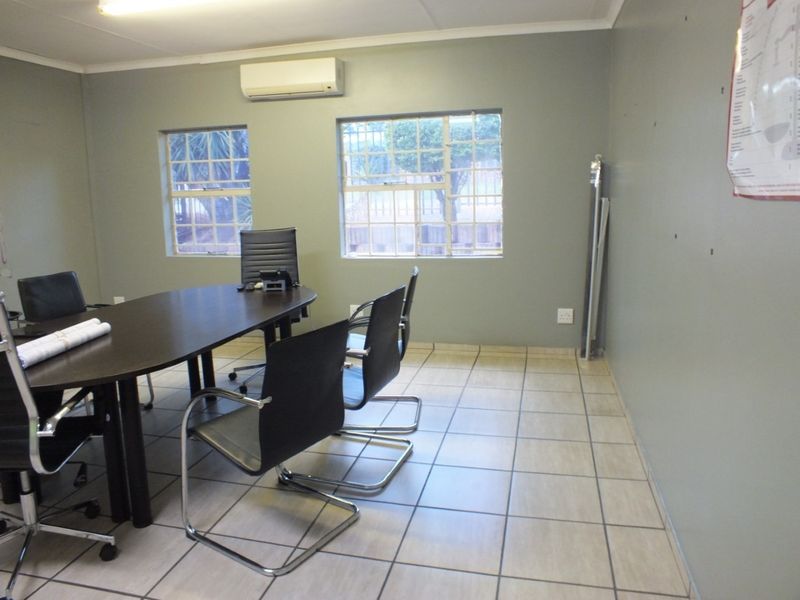 A functional office space featuring tiled flooring, split-system air conditioning, and large windows with security bars, suitable for a professional business environment.
