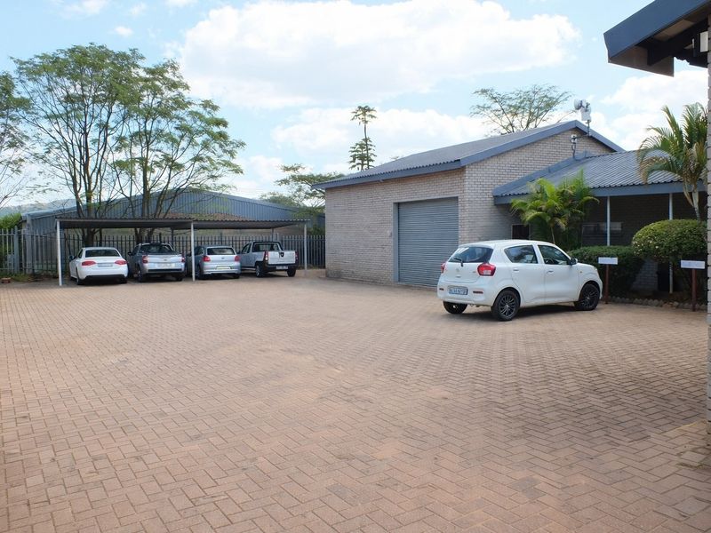 Spacious paved parking area featuring a covered carport and a building with a roller shutter door, suitable for business or commercial use.