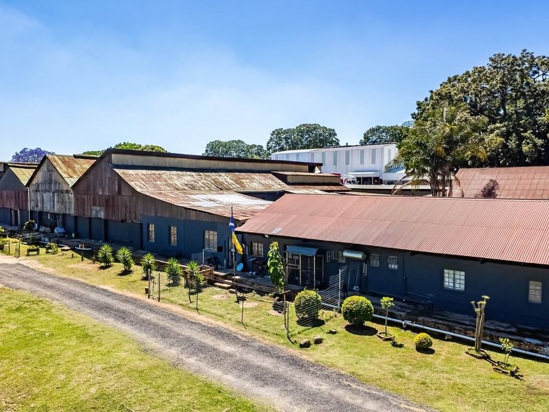 Aerial view of an industrial property complex featuring multiple warehouse structures with corrugated metal roofing and an adjacent gravel access road.