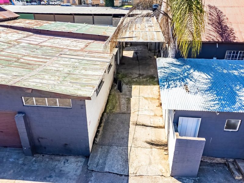 Aerial view of an industrial property featuring multiple structures with corrugated metal roofing, concrete driveway access, and roller shutter doors.