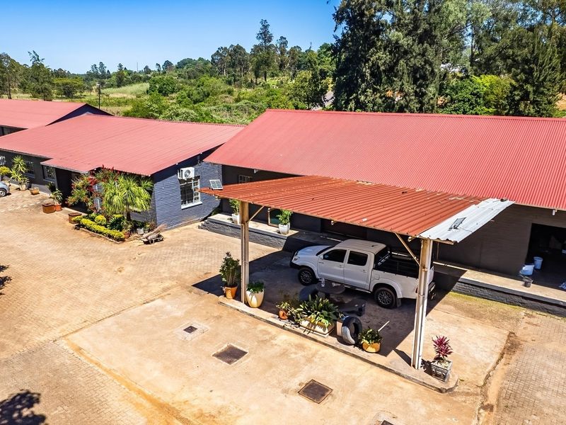 Aerial view of an industrial property featuring multiple buildings with corrugated metal roofs, paved driveway areas, and a covered carport structure.