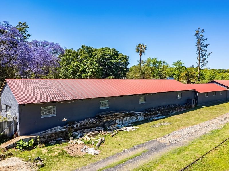 Aerial view of an industrial warehouse building featuring a red corrugated metal roof, glass block windows, and perimeter security fencing.