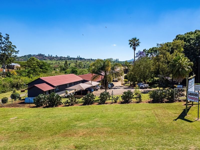 Aerial view of an industrial property featuring a metal-roofed building, paved driveway, and shade cloth carport set within a landscaped outdoor area.