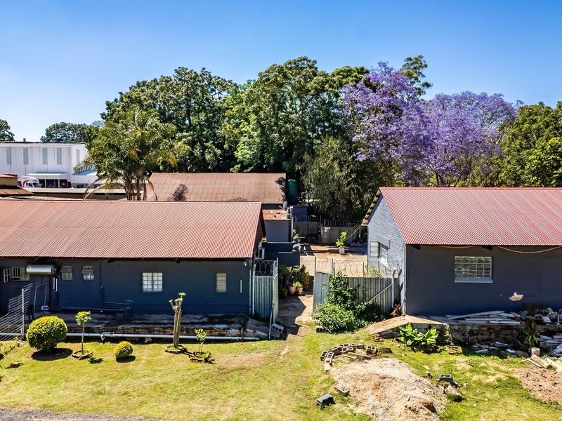 Aerial view of an industrial property featuring multiple structures with corrugated metal roofs, security fencing, and established garden areas.