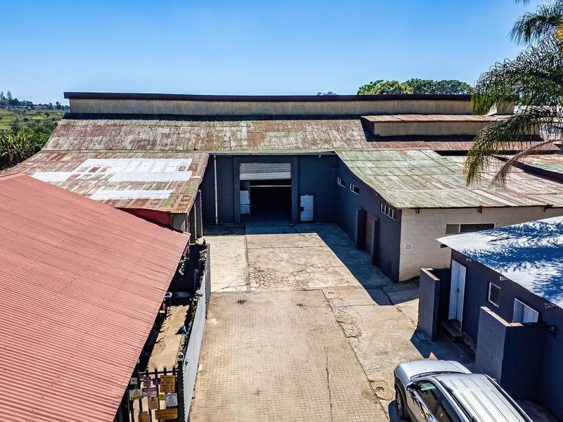 Aerial view of an industrial property featuring a large warehouse with corrugated metal roofing, a roller shutter door, and a paved yard area.