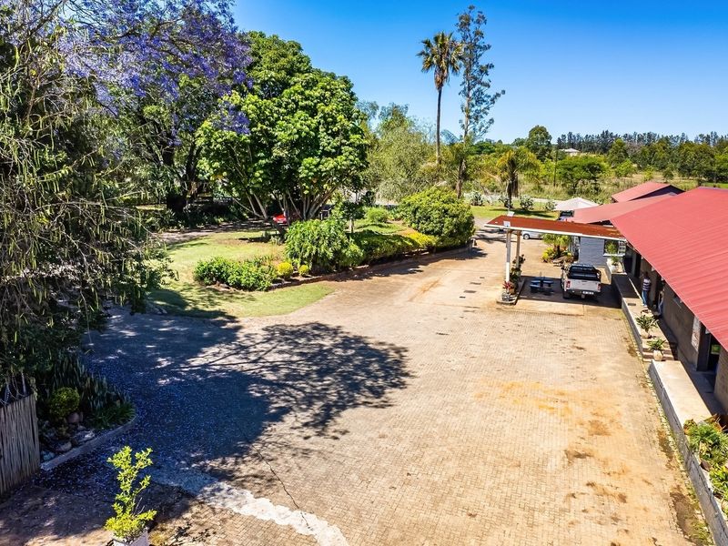 Aerial view of an industrial property featuring a large paved driveway, covered parking structure, and established garden surroundings.