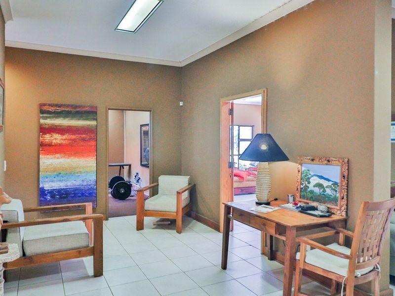 A spacious living area featuring neutral tiled flooring, coved cornicing, and recessed lighting, providing access to adjacent rooms within the guest house.