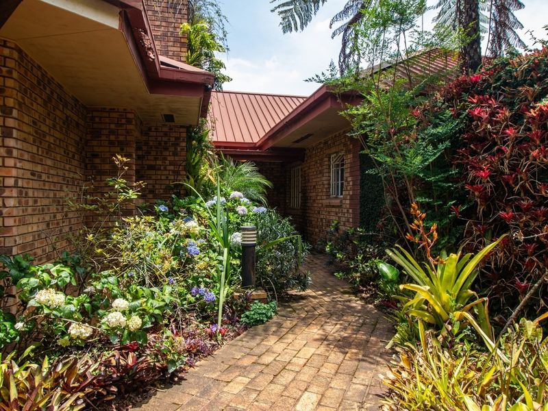 A well-maintained brick pathway leads through a lush, established garden between two sections of the face brick guest house structure.