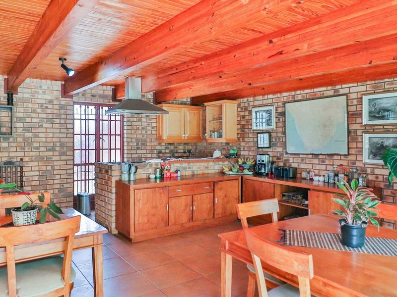 Open-plan kitchen and dining area featuring rustic brick walls, exposed timber ceiling beams, and warm wooden cabinetry with integrated cooking facilities.
