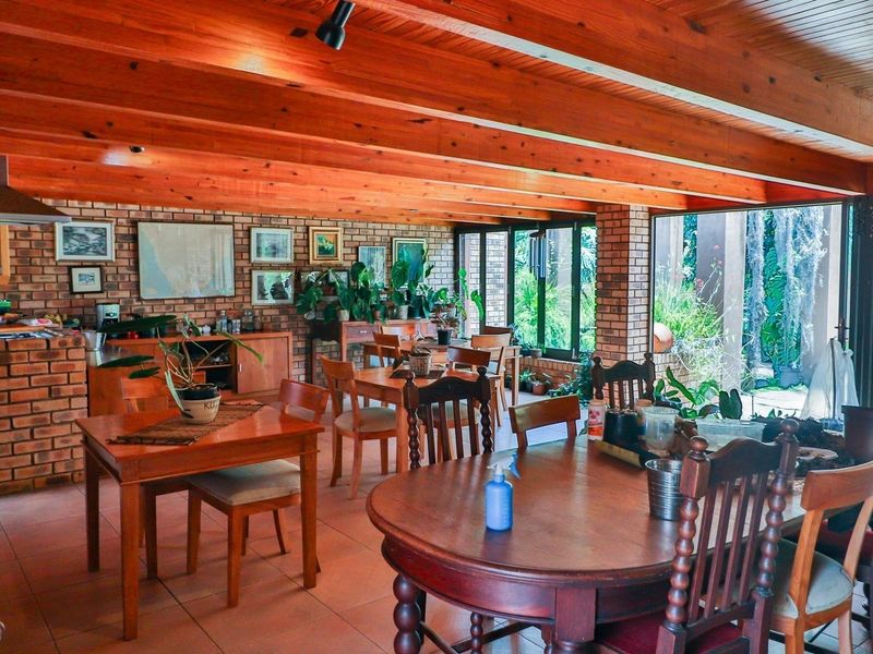 Spacious open-plan living and dining area featuring exposed timber beams, facebrick walls, and large glass doors opening to the garden.