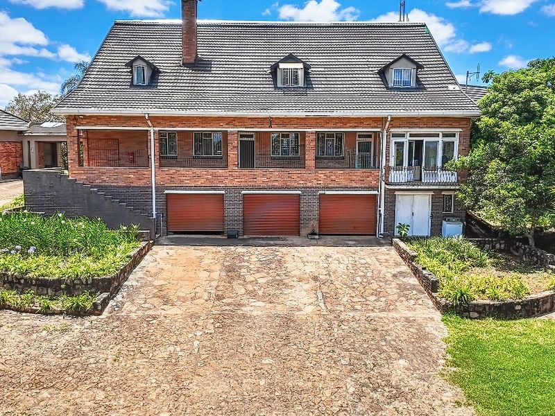 Front elevation of a multi-story brick farmhouse featuring a triple garage, stone driveway, and dormer windows set within a landscaped garden.