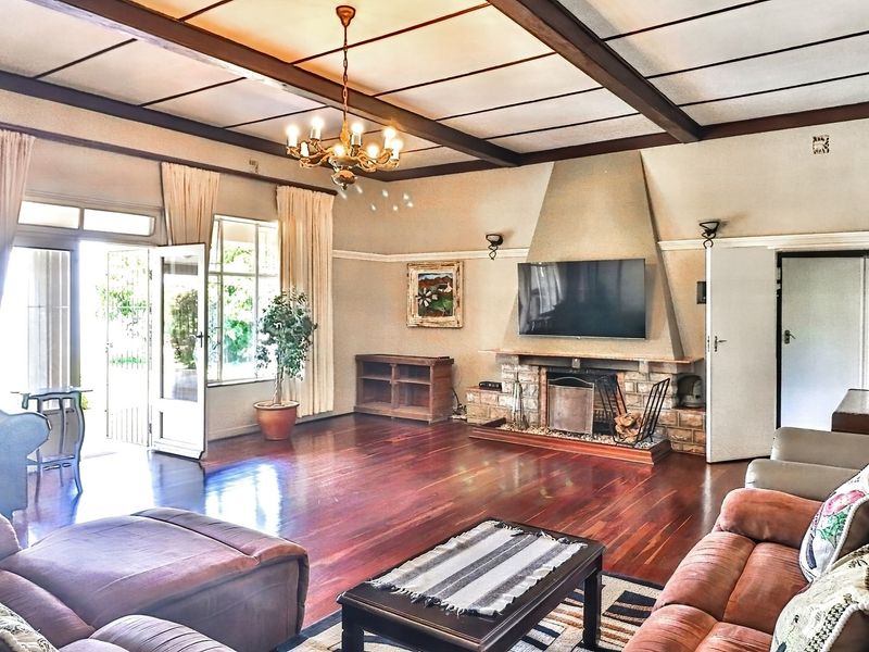 Spacious living room featuring exposed timber ceiling beams, hardwood flooring, and a prominent stone-clad fireplace with direct access to the garden through french doors.