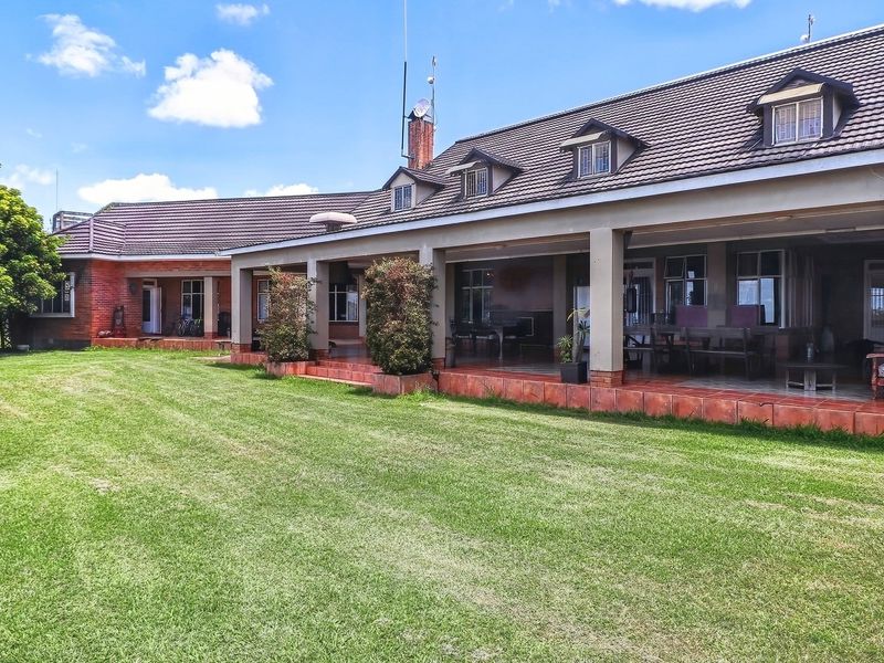 Spacious rear exterior view of the farm property featuring a large covered patio, tiled roof with dormer windows, and an expansive lawn area.