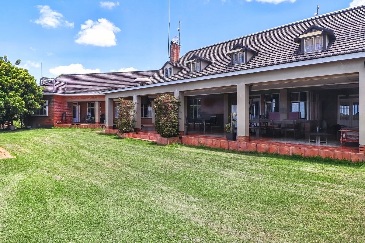 Spacious rear exterior view of the farm property featuring a large covered patio, tiled roof with dormer windows, and an expansive lawn area.