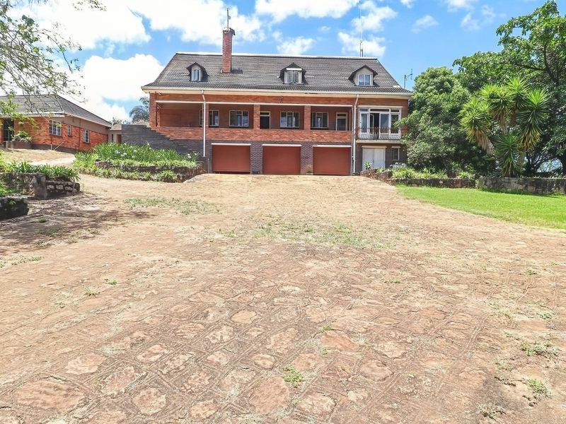 Front view of a multi-story brick farmhouse featuring a triple garage, covered patio, and a large stone driveway set on a spacious rural property.