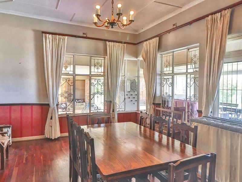 A traditional dining room featuring hardwood flooring, decorative ceiling molding, and large windows fitted with wrought iron security bars.