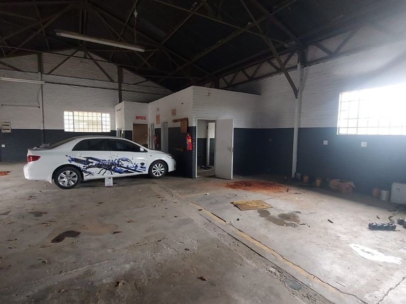 Spacious industrial utility area featuring exposed roof trusses, concrete flooring, and an integrated office partition, suitable for workshop or storage use.