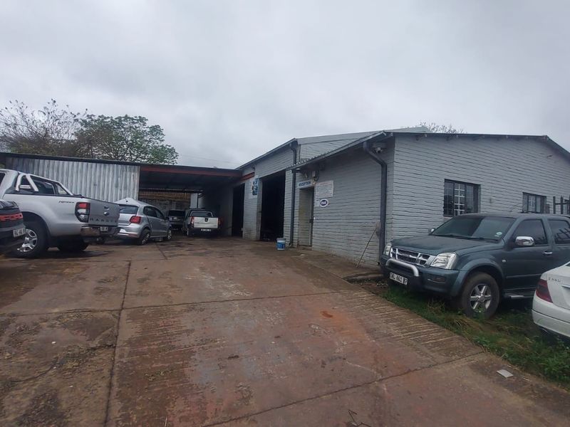 Industrial property exterior featuring a concrete driveway, covered parking area, and brick facade with security window bars.
