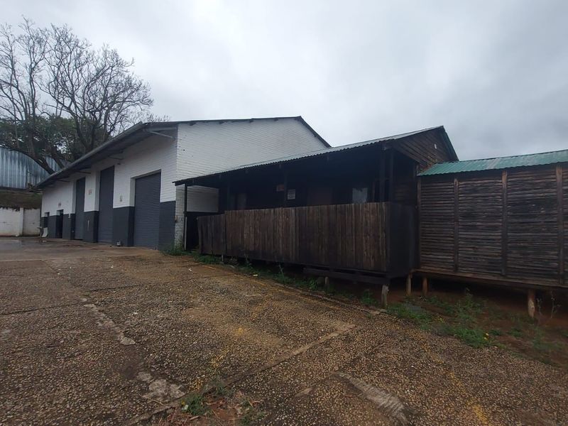 Rear view of an industrial property featuring a main warehouse structure with roller shutter doors and an adjacent timber-clad auxiliary building.