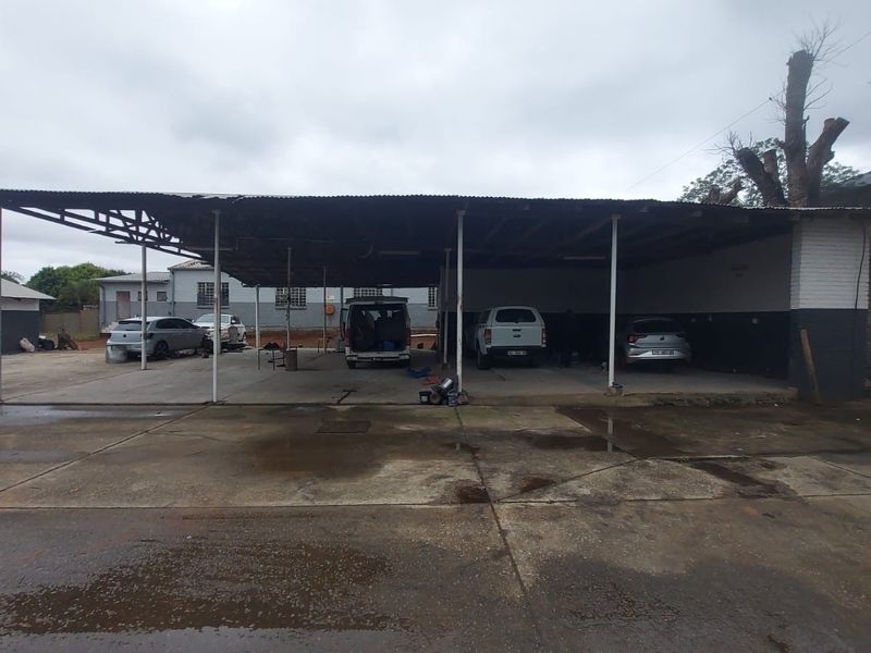 Large industrial outdoor covered parking or work area featuring a corrugated metal roof structure supported by steel columns over a concrete hardstand.