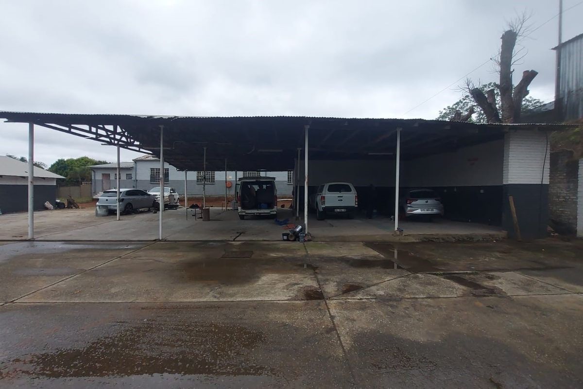 Large industrial outdoor covered parking or work area featuring a corrugated metal roof structure supported by steel columns over a concrete hardstand.
