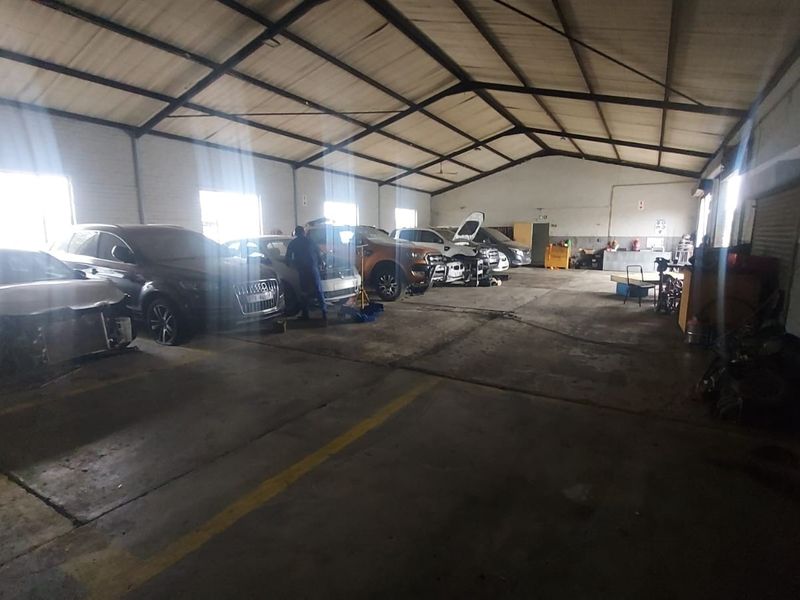 Spacious industrial garage facility featuring high exposed steel roof trusses, durable concrete flooring, and large roller shutter access points.