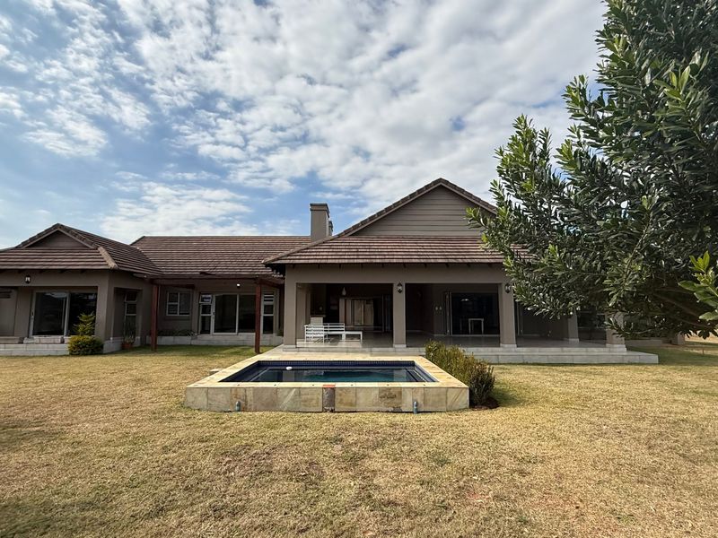 Rear view of the house featuring a covered patio, tiled roof, and a built-in swimming pool set within a landscaped garden.