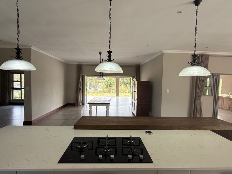 Spacious open-plan living area featuring a modern kitchen island with gas cooktop, pendant lighting, and seamless flow to an outdoor patio through bi-fold doors.