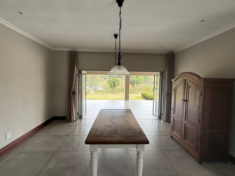 Spacious dining area featuring large format floor tiles, recessed lighting, and wide folding doors opening onto a covered patio and garden.