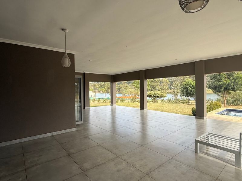 Spacious covered patio featuring large format floor tiles, recessed lighting, and direct access to the garden and pool area with scenic views.
