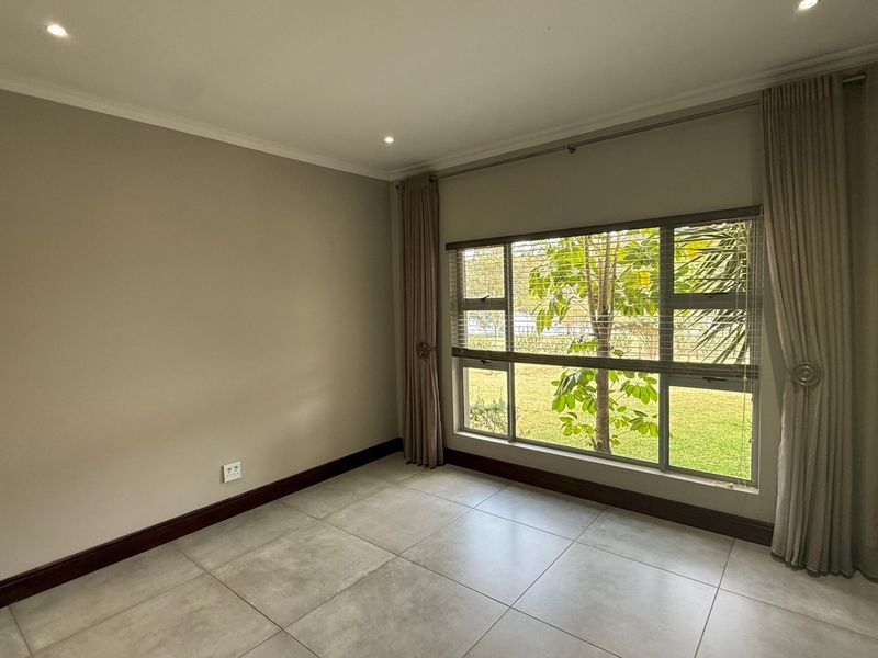A bright, empty bedroom featuring neutral tiled flooring, recessed downlighting, and large windows with garden views, providing a clean canvas for personalization.