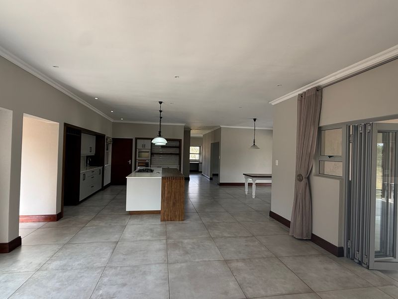 Spacious open-plan living and kitchen area featuring a central island, modern cabinetry, tiled floors, and large stacking doors leading to an outdoor space.