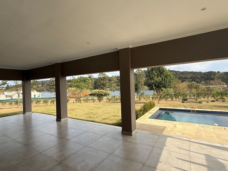 Spacious covered patio featuring tiled flooring and recessed lighting, overlooking a private swimming pool and expansive garden with scenic landscape views.