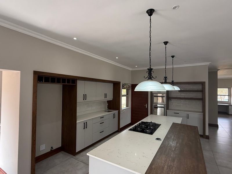 Modern kitchen featuring a large island with a gas hob, stone countertops, built-in oven, and ample cabinetry, finished with elegant pendant lighting.