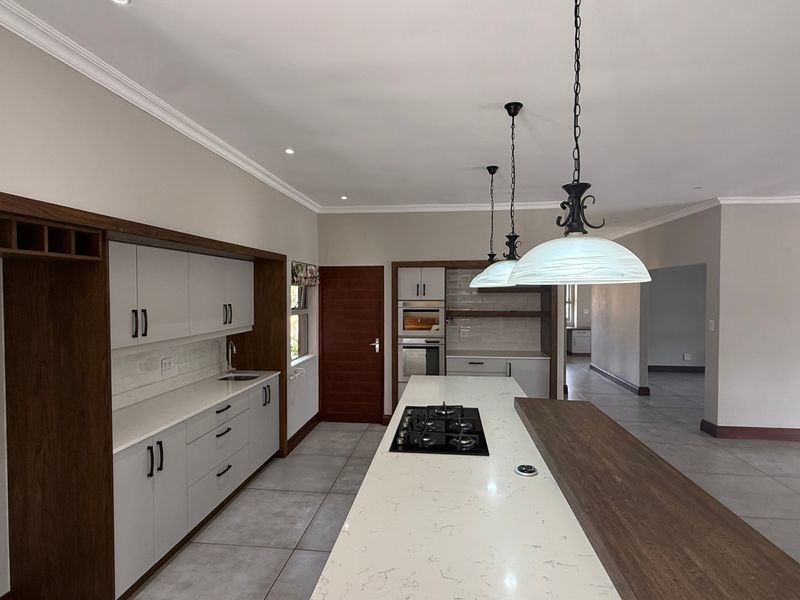 Modern kitchen featuring a large island with gas cooktop, stone countertops, built-in oven, and sleek cabinetry, offering a clean and functional culinary space.