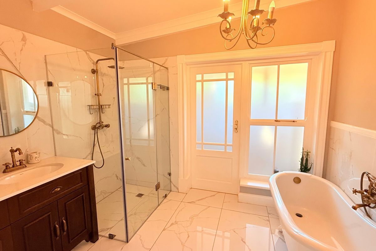 Elegant bathroom featuring a freestanding bathtub, glass-enclosed shower, marble-look tiling, and classic brass fixtures with direct access to an outdoor area.