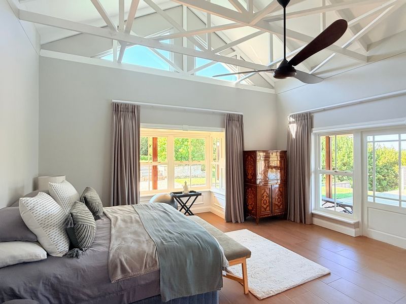 Spacious bedroom featuring high vaulted ceilings with exposed trusses, a ceiling fan, large bay windows, and direct access to the outdoor area via french doors.