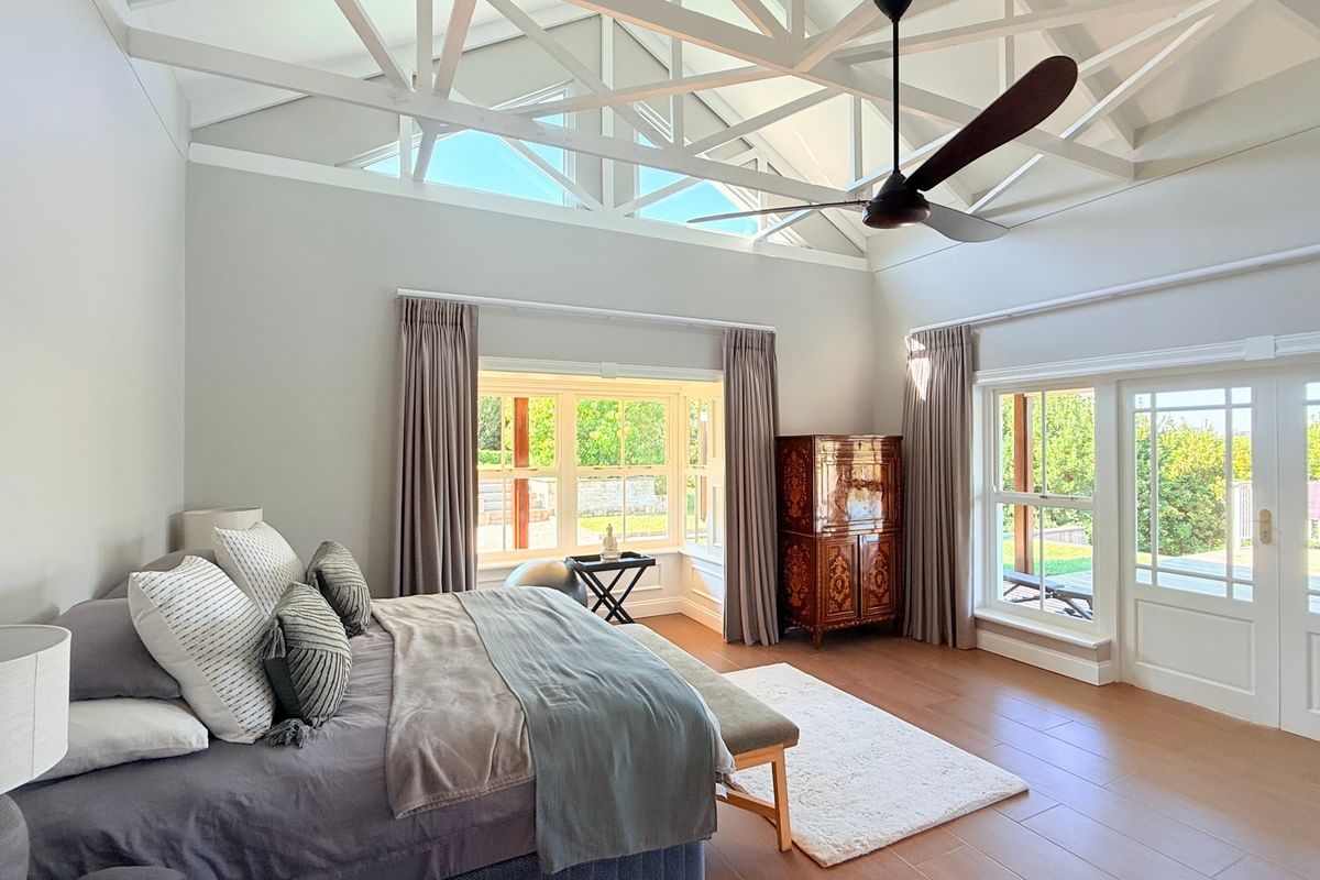 Spacious bedroom featuring high vaulted ceilings with exposed trusses, a ceiling fan, large bay windows, and direct access to the outdoor area via french doors.