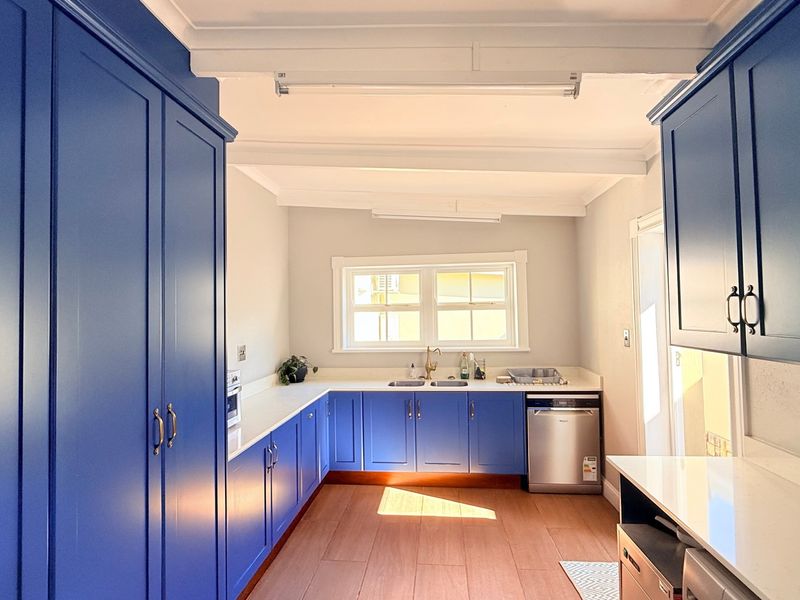 A modern, well-lit kitchen featuring vibrant blue cabinetry, stone countertops, integrated appliances, and timber-look flooring, offering a clean and functional workspace.