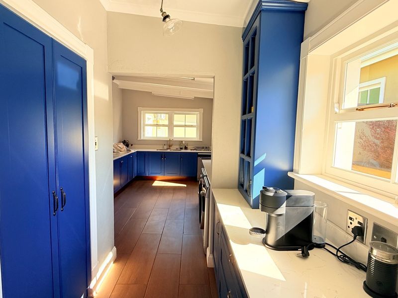 A bright, modern kitchen featuring vibrant blue cabinetry, stone countertops, and tiled flooring, with a seamless transition into an adjoining prep or scullery area.