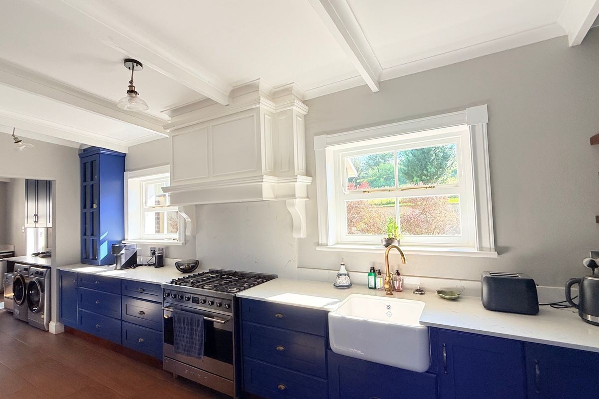 A well-appointed kitchen featuring blue cabinetry, stone countertops, a farmhouse sink, and a gas range with a custom extractor hood.