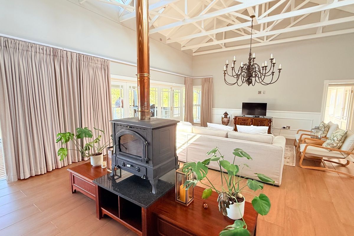Spacious living room featuring a vaulted ceiling with exposed trusses, a central wood-burning fireplace, wainscoting, and large sliding doors leading to an outdoor area.