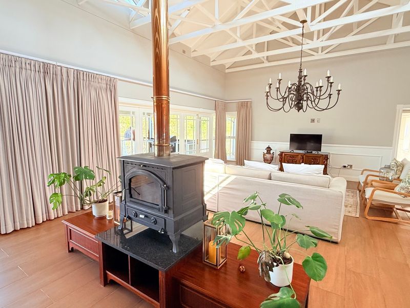 Spacious living room featuring a vaulted ceiling with exposed trusses, a central wood-burning fireplace, wainscoting, and large sliding doors leading to an outdoor area.