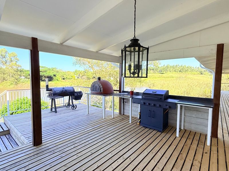 Spacious covered timber deck featuring a built-in outdoor kitchen area, pendant lighting, and scenic water views.