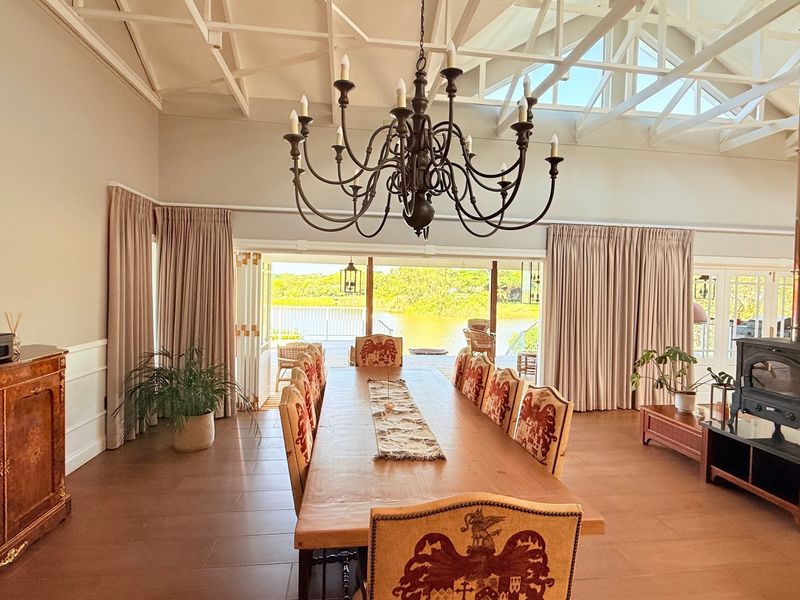 Spacious dining room featuring vaulted ceilings with exposed trusses, a wood-burning fireplace, and large stacking doors opening to a scenic outdoor view.