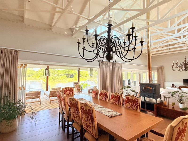 Spacious open-plan living and dining area featuring high exposed roof trusses, a wood-burning fireplace, and large sliding doors opening to a deck.