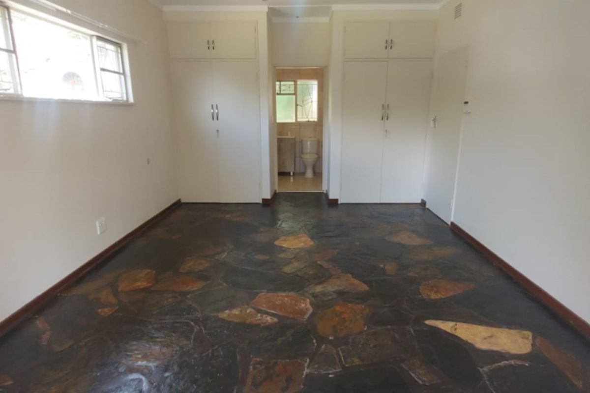 An empty bedroom featuring unique stone flooring, built-in cupboards, and an en-suite bathroom visible through the doorway.