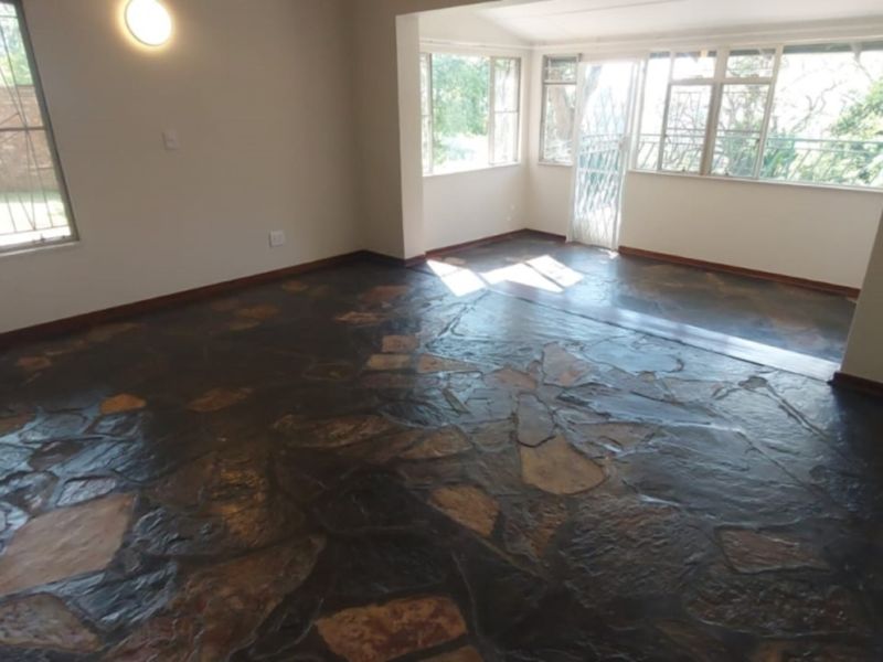 An empty living room featuring unique crazy paving stone flooring, large windows providing natural light, and a secure entrance gate.