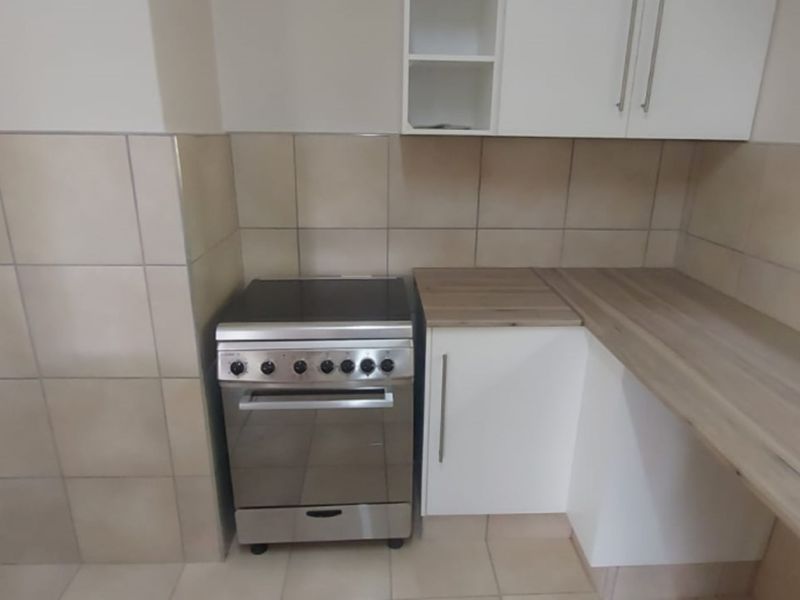 A clean, functional kitchen area featuring tiled splashbacks, built-in cabinetry, a freestanding stove, and ample laminate countertop space.