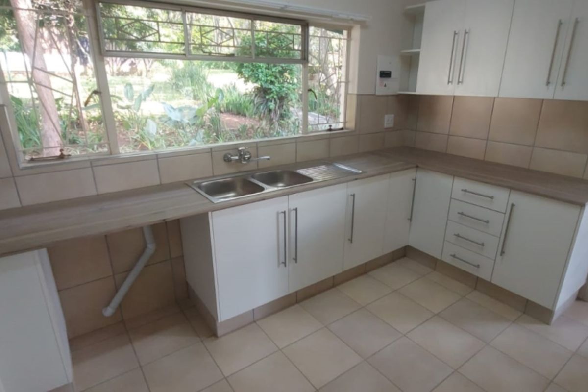 A clean, functional kitchen featuring white cabinetry, laminate countertops, tiled backsplash, and a double basin sink overlooking the garden.